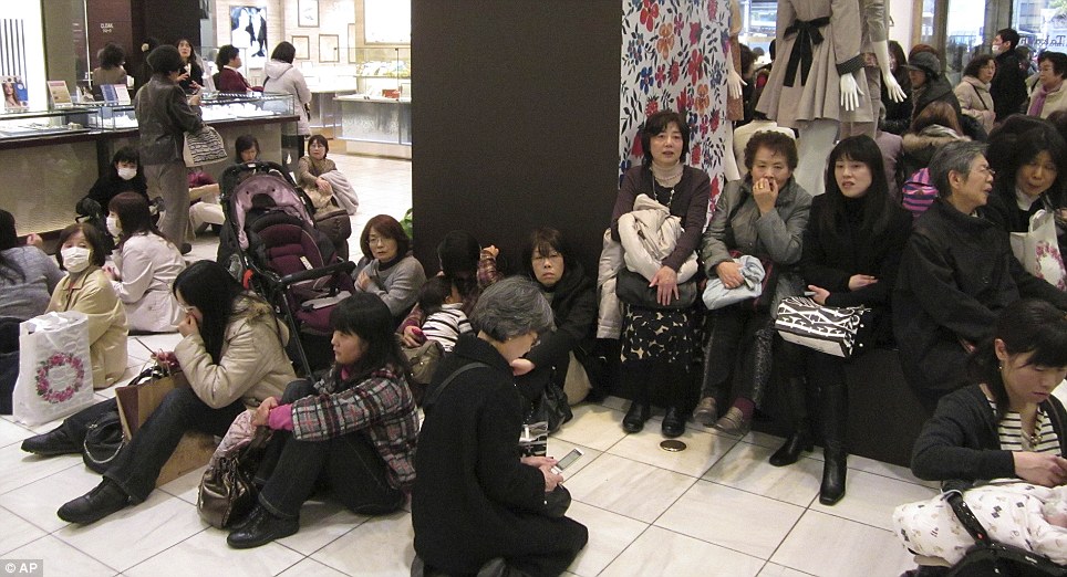 Stranded: Shoppers sit on the floor of a department store as train and bus services were suspended due to the earthquake